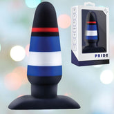 A black, red, blue, and white striped butt plug made from platinum-cured silicone is displayed against a background of multicolored lights. To the right, the same Avant Pride P4 Power Play Silicone Butt Plug is shown in its white box packaging labeled "PRIDE" with small icons and text on the side.